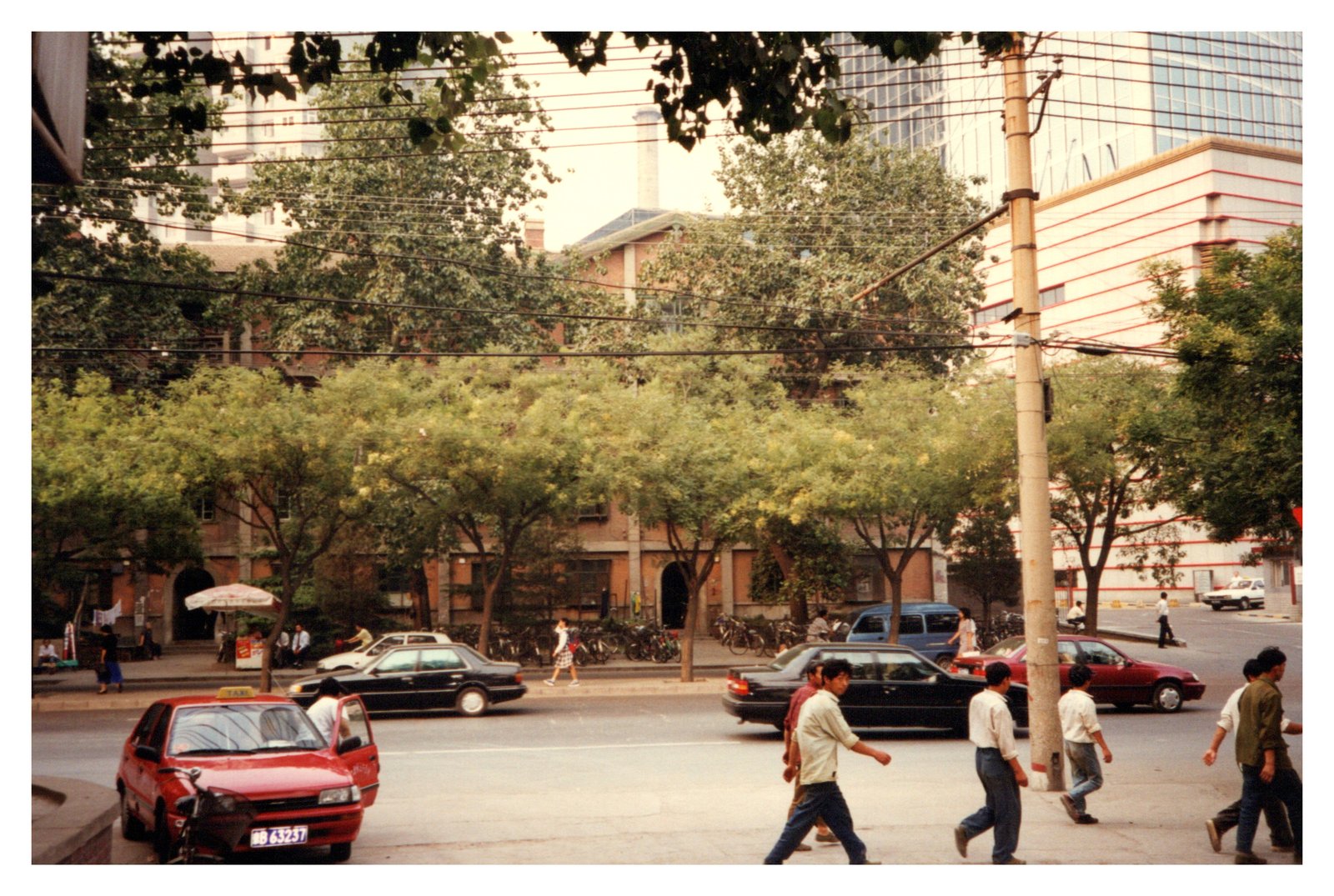 A Beijing street scene in the 1990s, with red car and pedestrians crossing